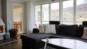Ein modernes Wohnzimmer mit einem dunkelgrauen Sofa, einem weißen Couchtisch und Blick auf eine Berglandschaft durch große Fenster.