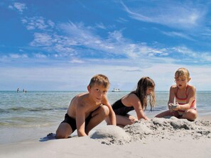 Tre barn leker på en sandstrand med havet i bakgrunden.
