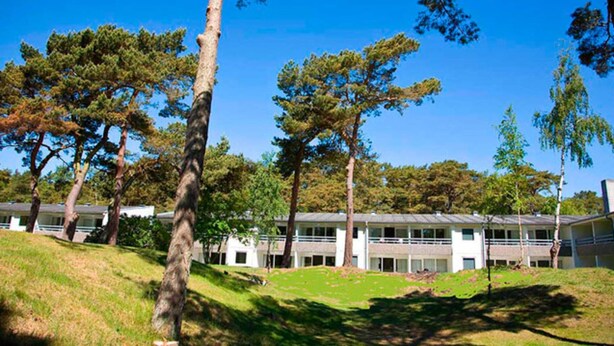 A building with a flat roof and multiple windows, surrounded by trees and a grassy area. - 2 Person Holiday Home in Nexo (Nexø)