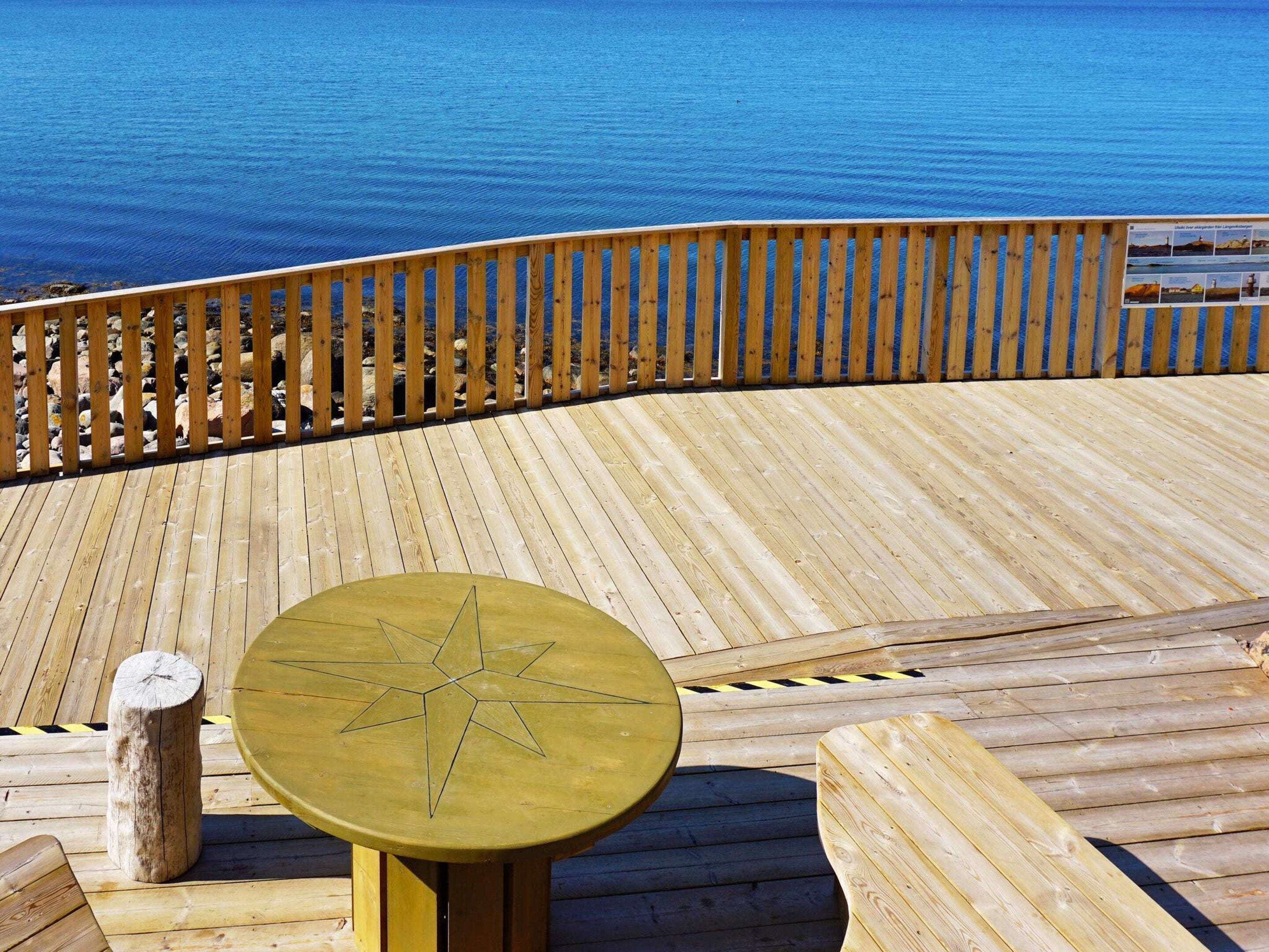 A wooden deck with a star-shaped table and benches, overlooking a body of water.