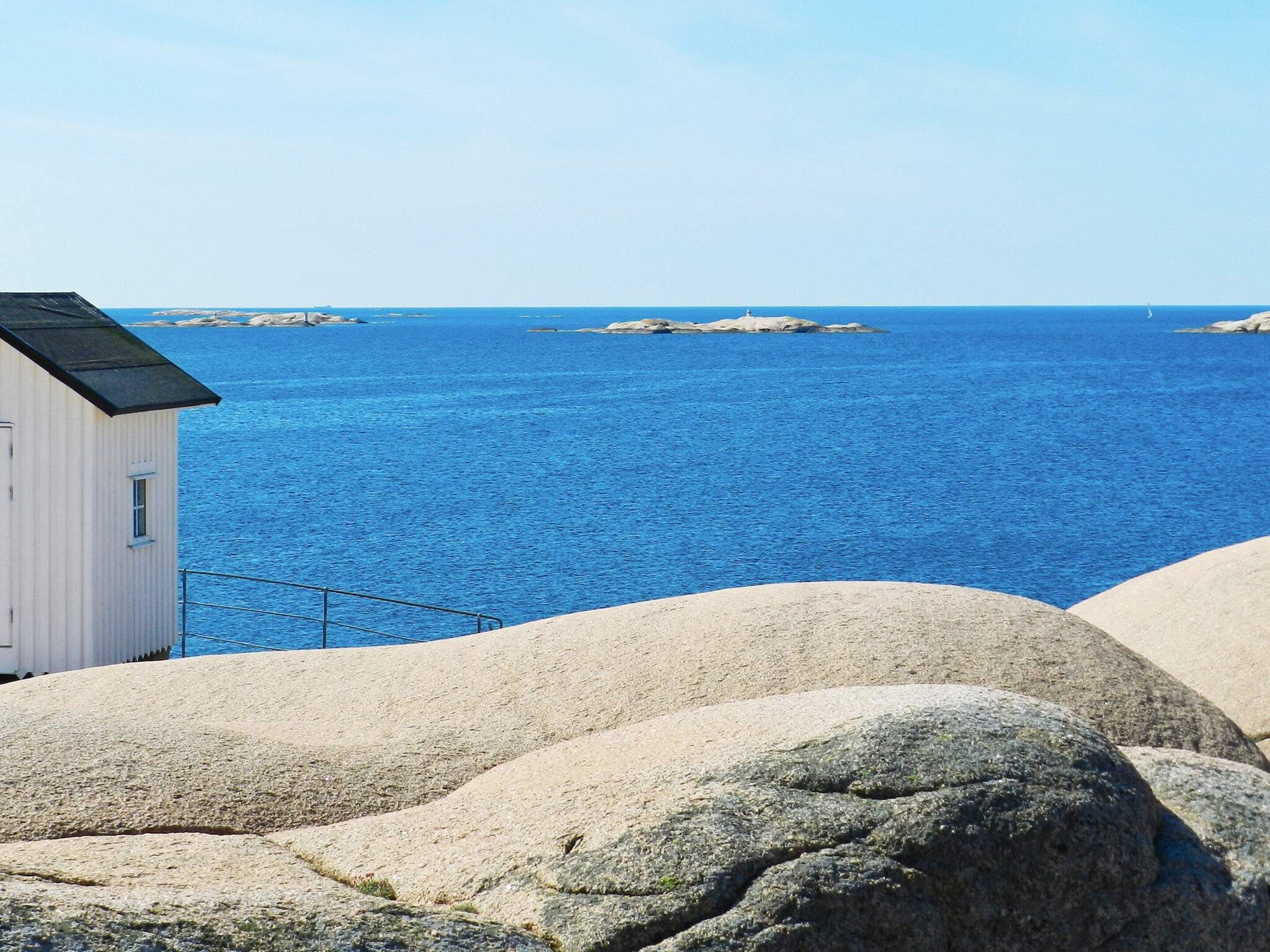 A coastal scene with a white building, large rocks, and a clear blue sea.