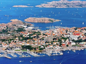 A coastal town with a marina, buildings with red roofs, and a rocky island in the background.