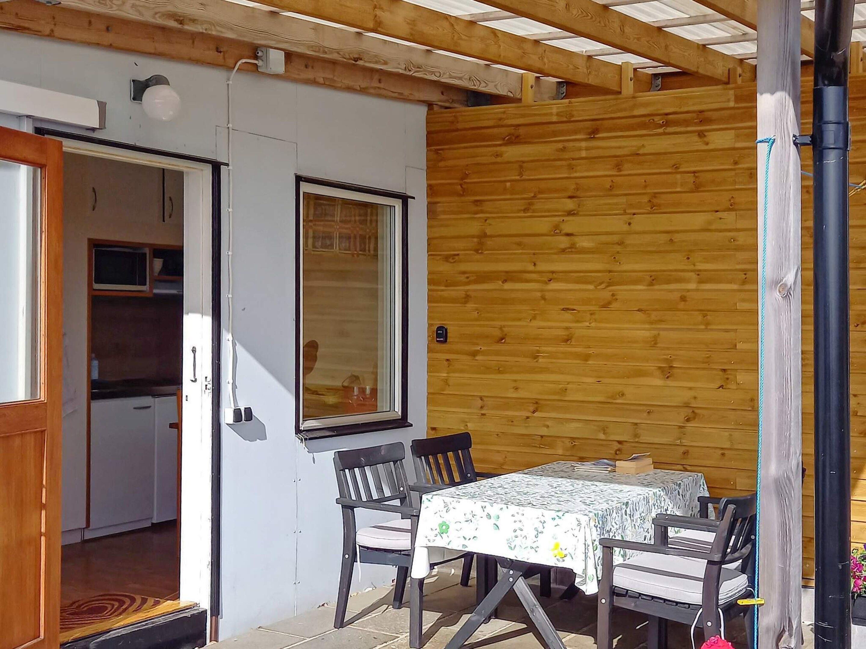 An outdoor patio with a table and chairs, a wooden wall, and a door leading to a kitchen area.