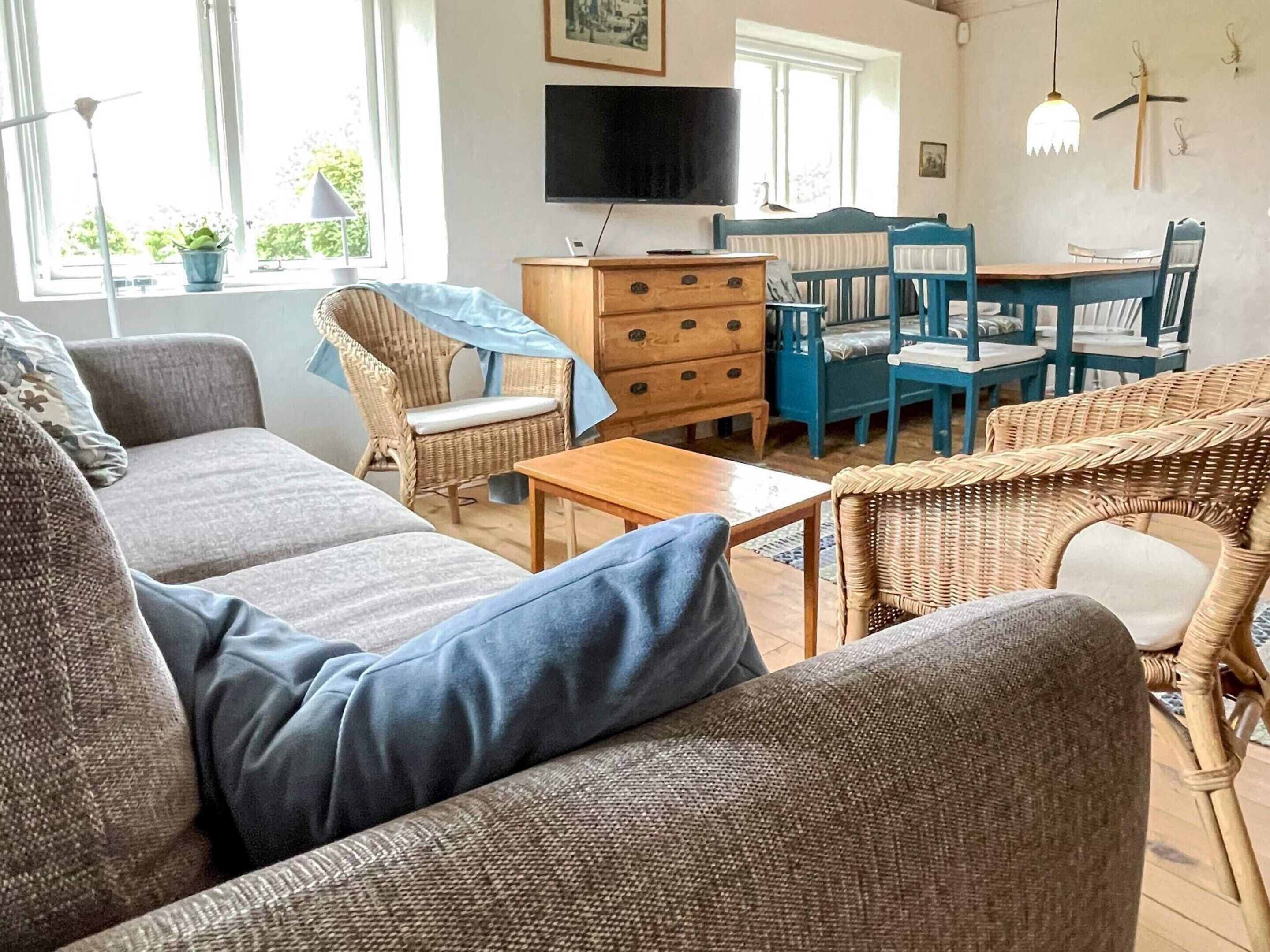 A furnished living room with a sofa, chairs, a wooden table, and a television.