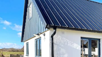 Een huis met een schuin metalen dak, een witte buitenmuur en een raam met een zwarte omlijsting.