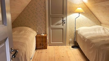 Een knus, klein zolderkamertje met twee bedden, een houten vloer en een deur met bloemenbehang.