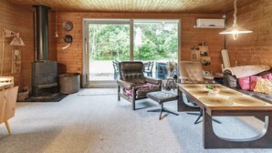 A cozy cabin interior with a fireplace, wooden ceiling, and a large sliding glass door leading to an outdoor area.