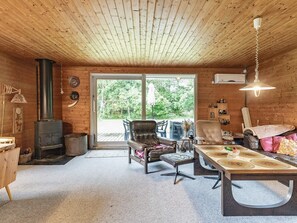 A cozy cabin interior with a fireplace, wooden ceiling, and a large sliding glass door leading to an outdoor area.