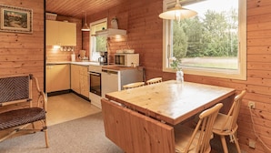 A wooden cabin interior with a kitchen, dining area, and a large window.