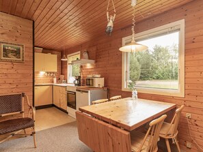 A wooden cabin interior with a kitchen, dining area, and a large window.