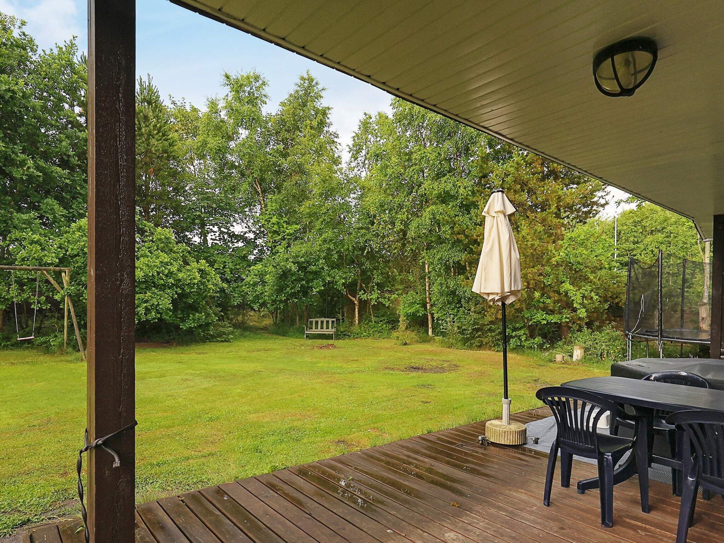 A covered outdoor area with a wooden deck, a bench, and a table with chairs.