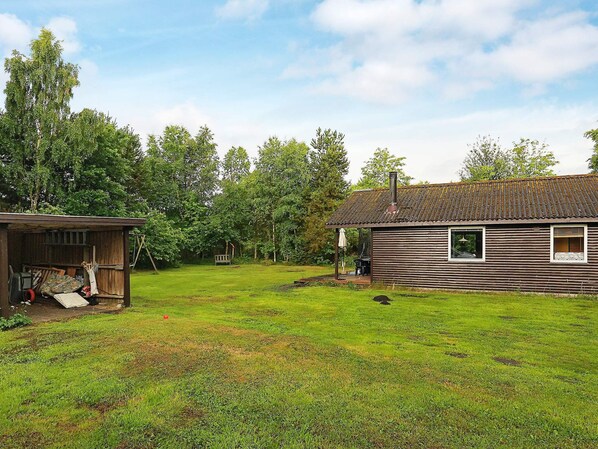 A rustic wooden cabin with a chimney, surrounded by a grassy yard and trees.