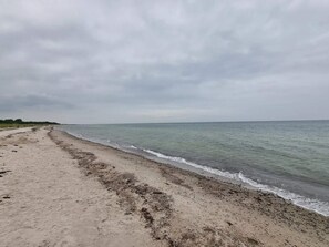 A sandy beach with gentle waves, a cloudy sky, and a distant shoreline.