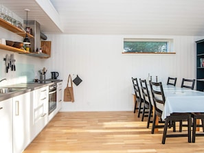 Una cocina moderna con armarios blancos, un comedor con mesa y sillas, y un ventanal con vistas a árboles.