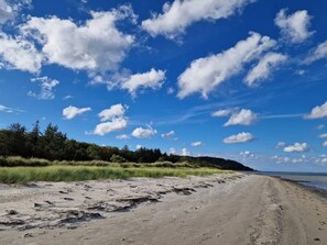 Uma praia arenosa com céu claro e nuvens esparsas.