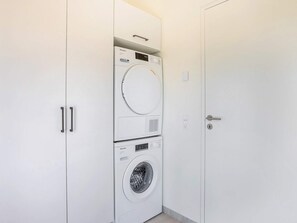A compact laundry room with a front-loading washer and dryer, a small control panel, and a door with a handle. - 5 Star Holiday Home in Hirtshals (Hirtshals)