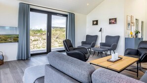 A modern living room with a large sliding glass door leading to a beach view, grey upholstered furniture, and a flat-screen TV mounted on the wall. - 5 Star Holiday Home in Hirtshals (Hirtshals)