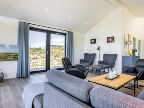 A modern living room with a large sliding glass door leading to a beach view, grey upholstered furniture, and a flat-screen TV mounted on the wall. - 5 Star Holiday Home in Hirtshals (Hirtshals)