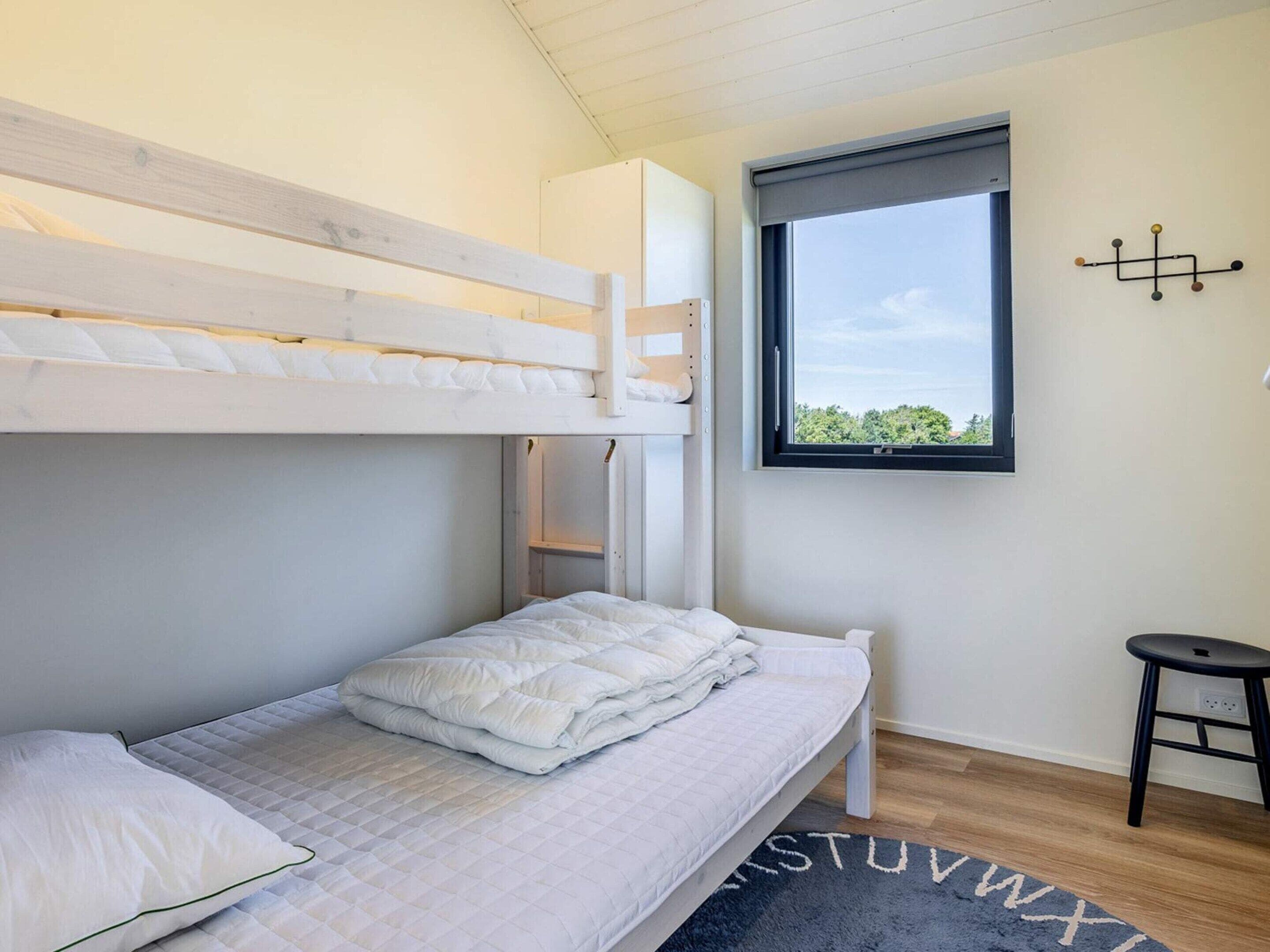 A bunk bed with a lower bed, a window with a view, and a small stool.