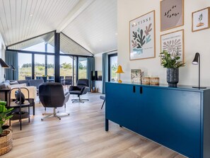 A modern living room with a blue cabinet, a sofa, and a dining area with a view through large windows. - 5 Star Holiday Home in Hirtshals (Hirtshals)