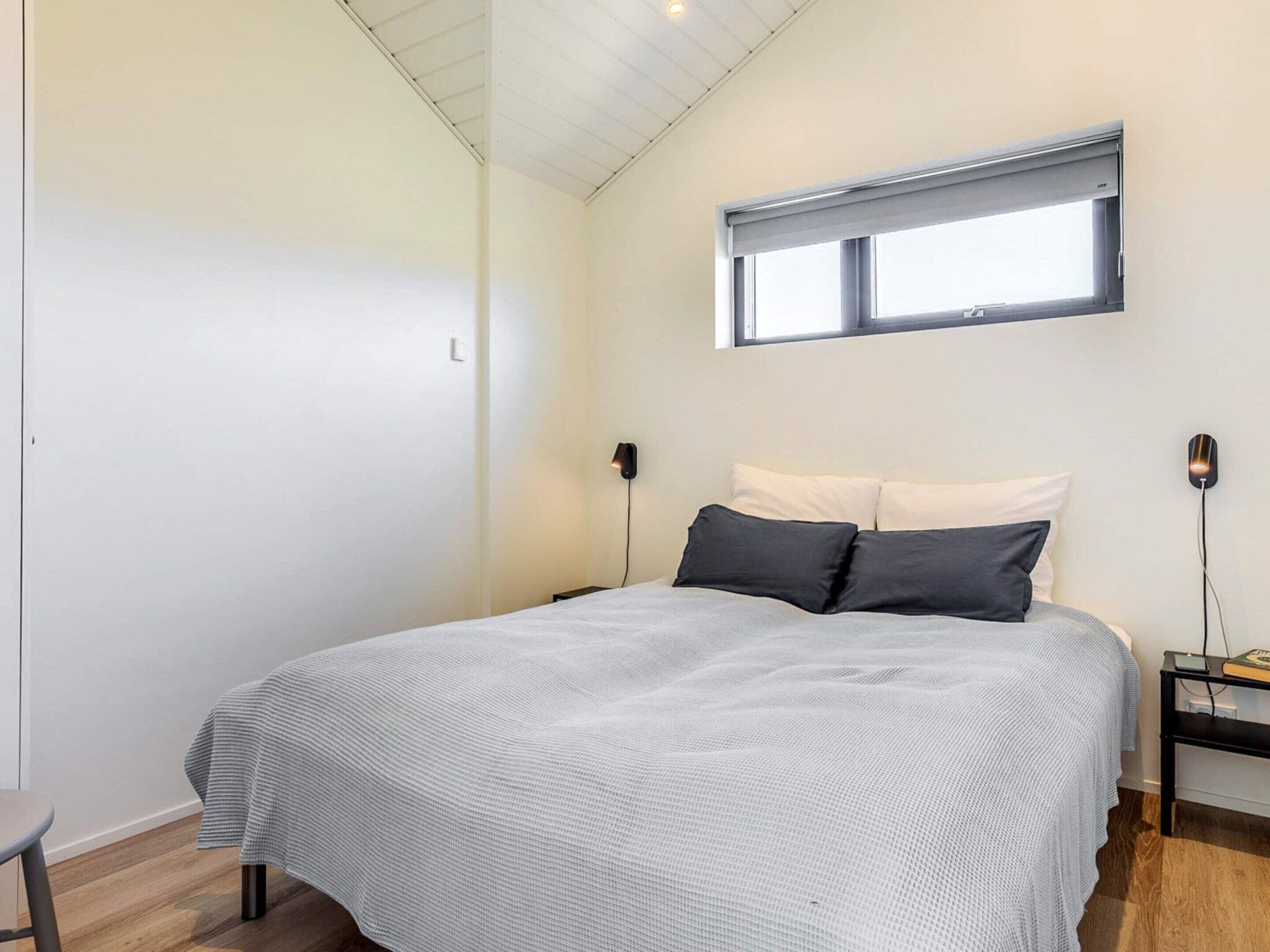 Un dormitorio con cama, dos mesitas de noche, una ventana y una lámpara en el techo.
