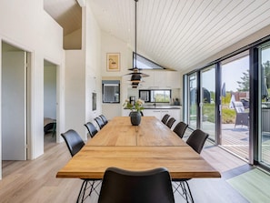 A modern dining area with a large wooden table, black chairs, and a kitchen in the background. - 5 Star Holiday Home in Hirtshals (Hirtshals)