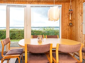 A dining area with a round table and chairs, large windows with a view of a lake, and wooden walls.