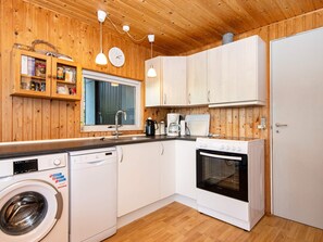 A compact kitchen with wooden walls, a washing machine, a coffee maker, and a stove. - 4 Person Holiday Home in Aabenraa (Aabenraa)