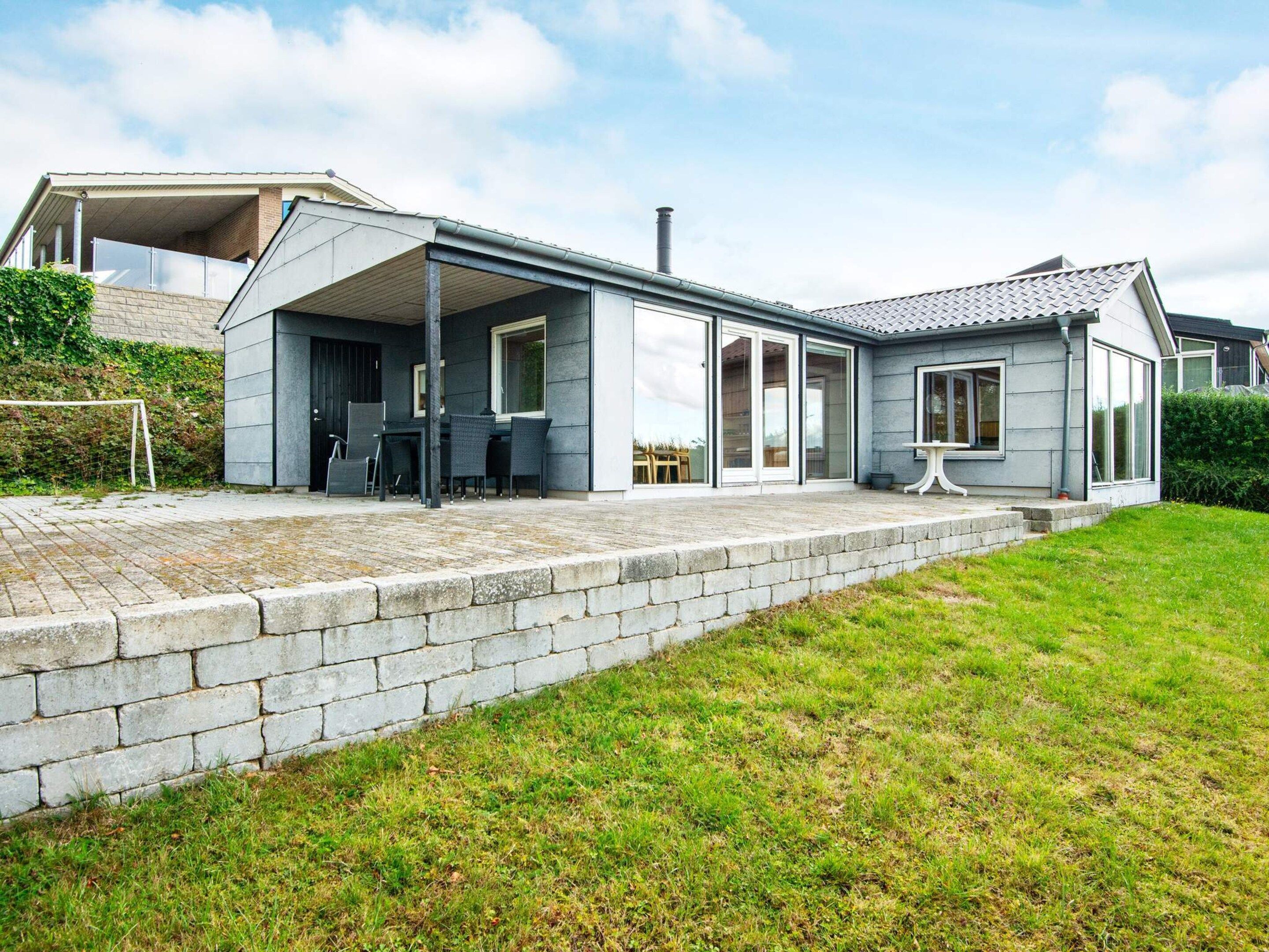 A modern house with a covered patio, a brick wall, and a grassy lawn.