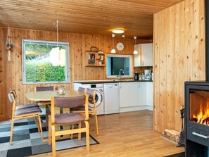 A cozy cabin interior with a dining area, kitchen, and a wood-burning stove.