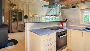 A modern kitchen with wooden cabinetry, a built-in oven, and a large window providing natural light. - Luxury Retreat by Kramnitze - By Traum Ferienwohnungen (Rodby)