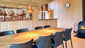 A wooden interior with a dining table, chairs, pendant lights, a clock, and a fireplace. - Luxury Retreat by Kramnitze - By Traum Ferienwohnungen (Rodby)