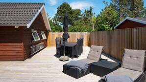 A wooden deck with outdoor furniture, including a table and chairs, and a covered umbrella. - Luxury Retreat by Kramnitze - By Traum Ferienwohnungen (Rodby)