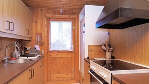 A compact kitchen with wooden cabinets, a stove, and a window with lace curtains. - 5 Person Holiday Home in Follenslev (Follenslev)