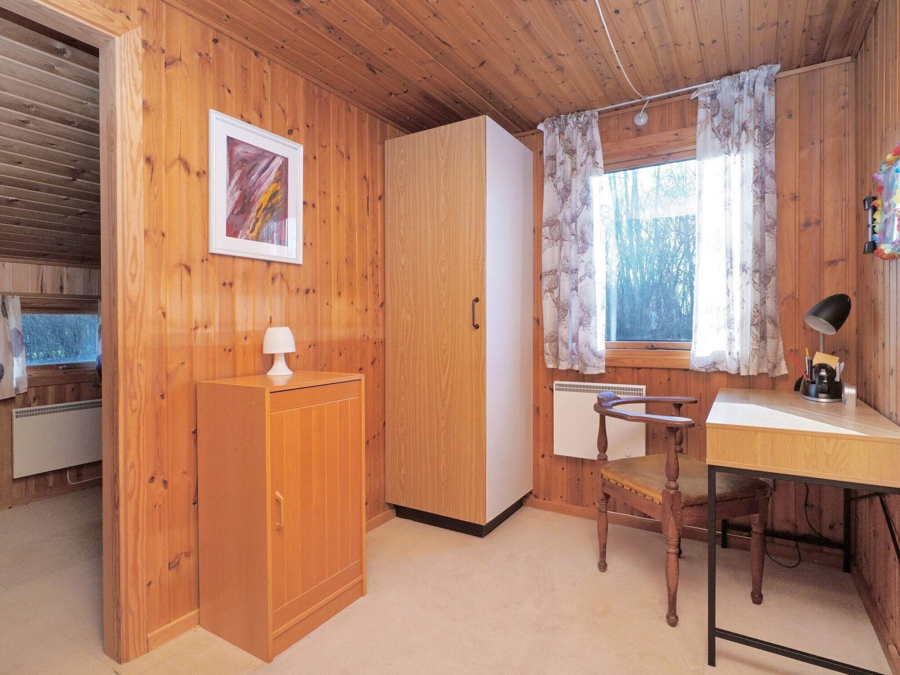 Een gezellig chalet met houten wanden, een bureau met stoel, een radiator en een raam met gordijnen.