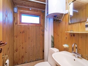 Un baño con paneles de madera, una ventana, ducha, lavamanos e inodoro.