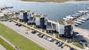 Un hôtel de bord de mer à l’architecture moderne, une marina avec des bateaux et une route bordée de voitures garées.