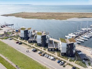 A coastal hotel with modern architecture, a marina with boats, and a road with parked cars. - 5 Star Holiday Home in Wendtorf (Wendtorf)