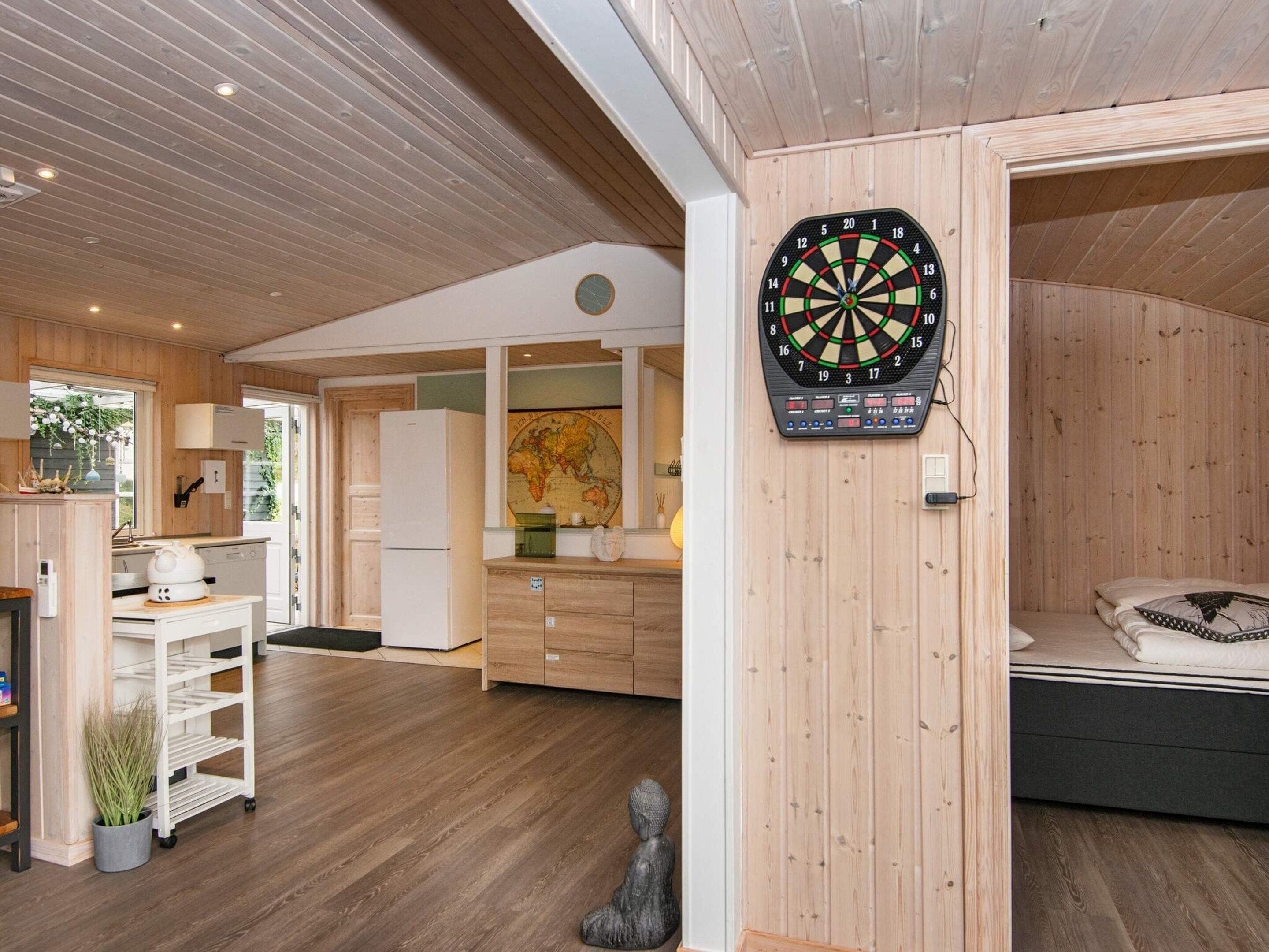 A modern interior with a dartboard, wooden flooring, a kitchen area, and a bed.