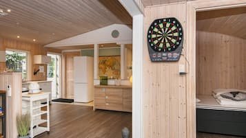 A modern interior with a dartboard, wooden flooring, a kitchen area, and a bed.