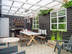 Een overdekt terras met een tafel, stoelen en een bank.