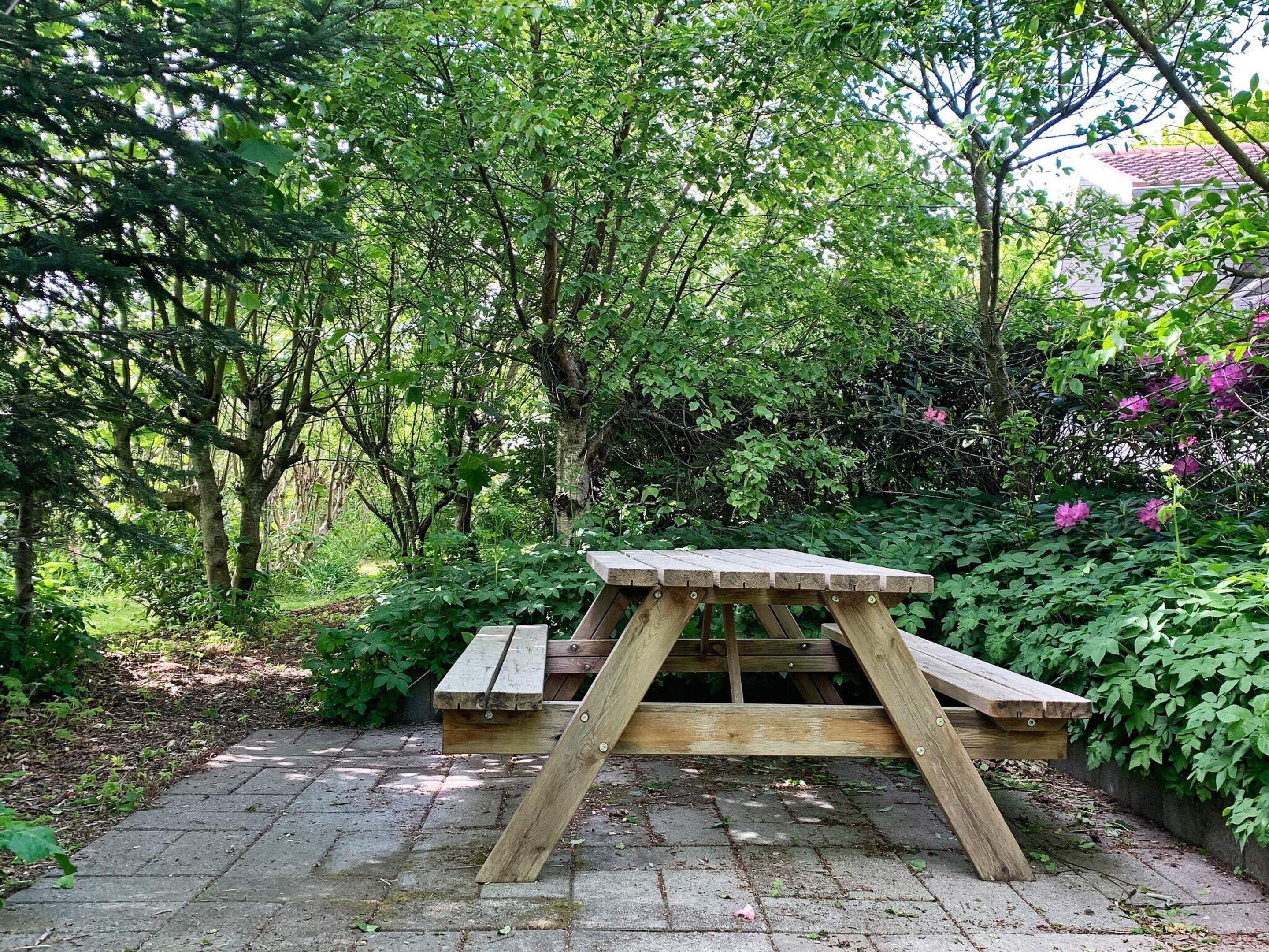 Una mesa de picnic de madera en un jardín con un camino de ladrillo.