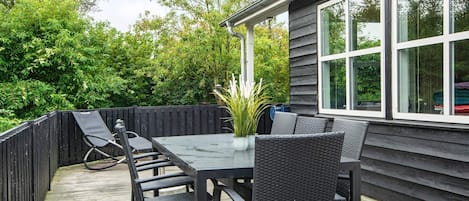 Un patio exterior con una mesa y sillas, rodeado por una terraza de madera y una valla negra.