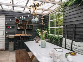 A rustic outdoor dining area with a wooden bench, a metal table, and various decorative items including a vase with flowers and lanterns.