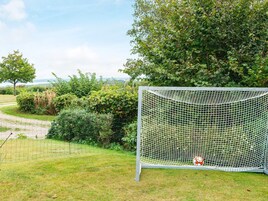 A soccer goal in a grassy area with a net, surrounded by greenery and a tree.
