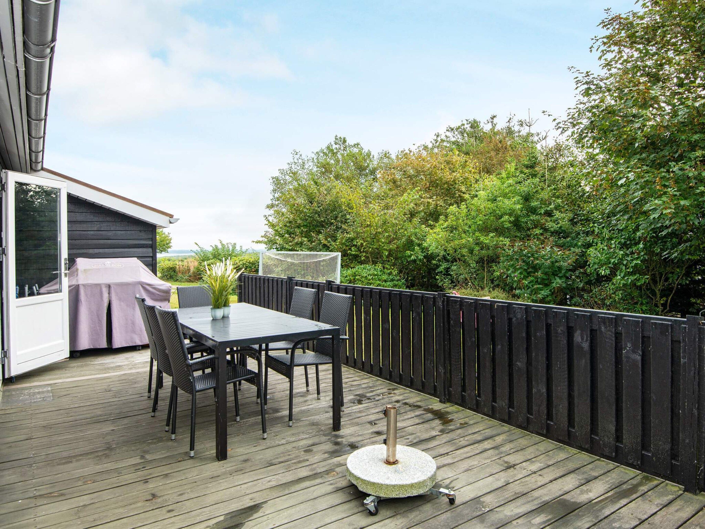An outdoor deck with a table and chairs, a covered grill, and a wooden fence.