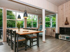 A spacious dining area with a wooden table and chairs, large windows, and a television. - 6 Person Holiday Home in Struer (Struer)
