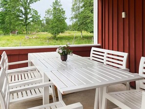 Une table et des chaises blanches sont disposées sur une véranda, offrant une vue sur un paysage verdoyant.