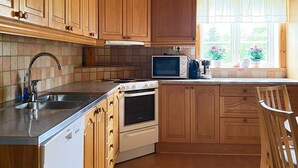 A kitchen with wooden cabinets, a stove, a microwave, and a sink. - 8 Person Holiday Home in Virestad (Virestad)