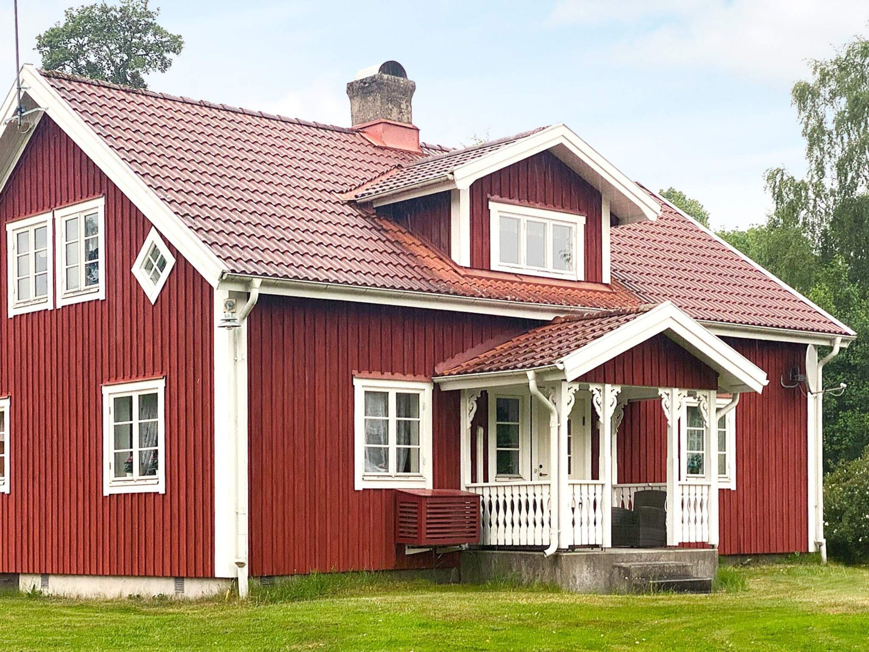 Ein rotes Holzhaus mit Satteldach, weißem Zierdekor und einer Veranda mit weißen Geländern.